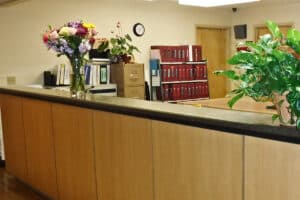 Nurses' desk with flowers and plants on it and a bookcase of folders behind.