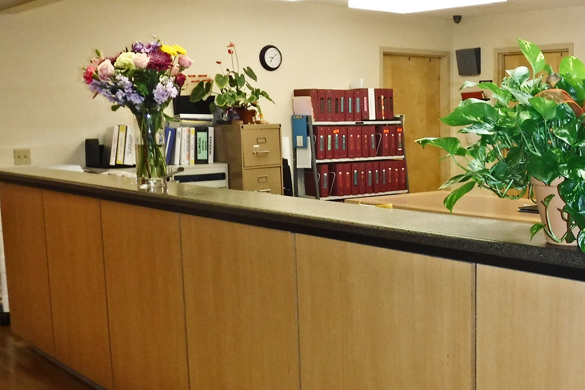 Nurses' desk with flowers and plants on it and a bookcase of folders behind.