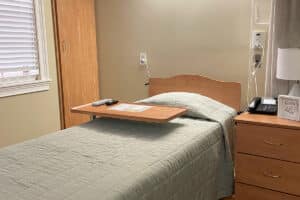 Close up of single occupancy room bed with phone and lamp on the nighstand.