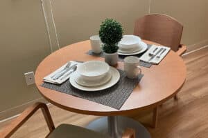 Dining table set with placemats, white dishware, and topiary.